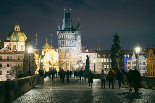 Prague Czechia 03 November 2021 View of Charles Bridge at night with historic statues illuminated gothic towers and people walking along the cobblestone path. Prague Czechia 03 November 2021 View of Charles Bridge at night with historic statues illuminated gothic towers and people walking along the cobblestone path.