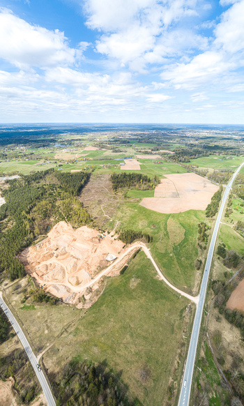 Aerial view of a sand quarry surrounded by lush green fields dense forests and intersecting roads under a bright blue sky in Latvia. Aerial view of a sand quarry surrounded by lush green fields dense forests and intersecting roads under a bright blue sky in Latvia.