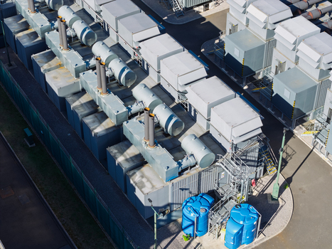 Aerial view of a data center facility featuring industrial cooling units ventilation systems and large blue water storage tanks on a paved site in the United Kingdom.