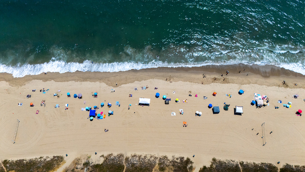 Aerial view of Will Rogers State Beach with colorful umbrellas people relaxing on the sand and ocean waves crashing on the shore in Los Angeles California United States.