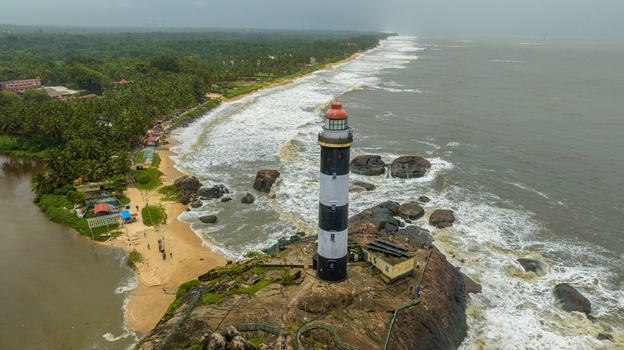 Aerial view of the iconic black and white striped Kapu Light House standing on a rocky outcrop overlooking the turbulent waves and sandy coastline in Udupi Karnataka India.