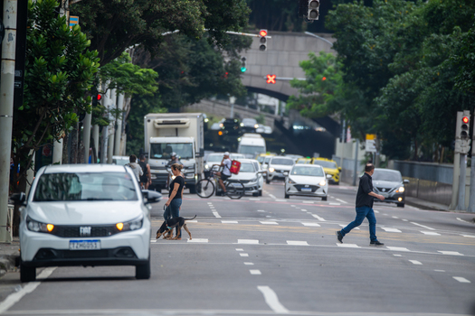 Rio de Janeiro Brazil 13 June 2026 View of pedestrians crossing a busy urban street with cars a white truck and a tunnel entrance surrounded by lush green trees.