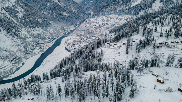 Aerial view of a snow laden valley with a winding river cutting through the landscape surrounded by dense pine forests and scattered dwellings Sharda Azad Kashmir Pakistan. Aerial view of a snow laden valley with a winding river cutting through the landscape surrounded by dense pine forests and scattered dwellings Sharda Azad Kashmir Pakistan.