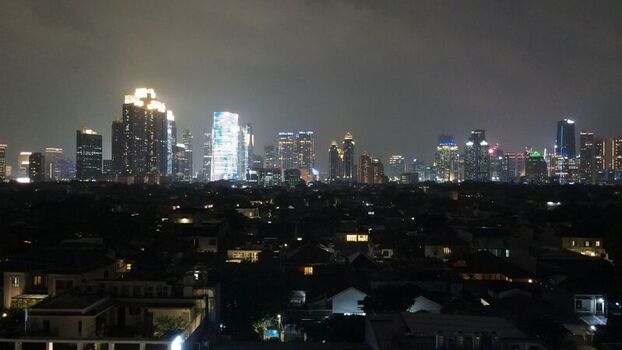 Aerial view of the illuminated South Jakarta skyline at night featuring modern skyscrapers rising above residential rooftops under a dark cloudy sky in South Jakarta Jakarta Indonesia. Aerial view of the illuminated South Jakarta skyline at night featuring modern skyscrapers rising above residential rooftops under a dark cloudy sky in South Jakarta Jakarta Indonesia.