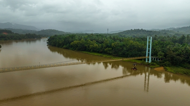 Aerial view of the suspension bridge spanning the Sharavathi River surrounded by lush green vegetation and hills under a cloudy sky in Honnavar Karnataka India.
