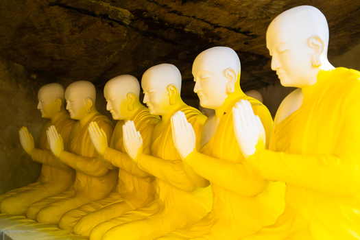 View of a row of Buddhist monk statues in yellow robes with hands in prayer position inside a cave at Adam s peak Ratnapura Sabaragamuwa Province Sri Lanka. View of a row of Buddhist monk statues in yellow robes with hands in prayer position inside a cave at Adam s peak Ratnapura Sabaragamuwa Province Sri Lanka.