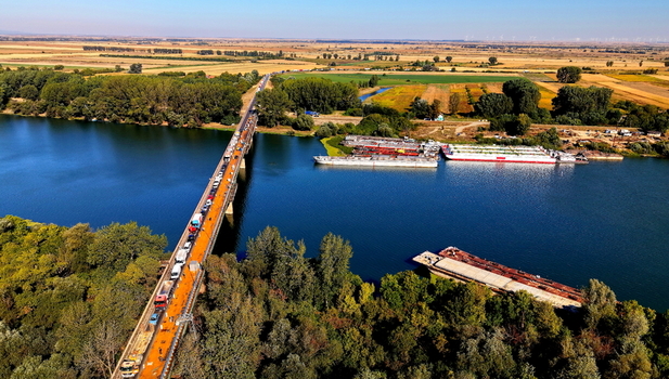 Aerial view of the Smederevo bridge with traffic and the nearby shipyard with barges on the river surrounded by lush greenery and fields in Smederevo Podunavlje District Serbia. Aerial view of the Smederevo bridge with traffic and the nearby shipyard with barges on the river surrounded by lush greenery and fields in Smederevo Podunavlje District Serbia.
