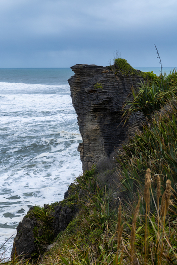 View of rugged cliffs meet the turbulent sea under a cloudy sky where dark rocks contrast with the white foam of crashing waves Pancake Rocks and Blowholes Walk West Coast Region New Zealand. View of rugged cliffs meet the turbulent sea under a cloudy sky where dark rocks contrast with the white foam of crashing waves Pancake Rocks and Blowholes Walk West Coast Region New Zealand.