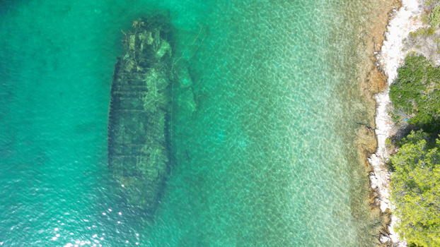Aerial view of a submerged shipwreck in turquoise clear waters near a rocky coastline with green trees in Necujam Split Dalmatia County Croatia. Aerial view of a submerged shipwreck in turquoise clear waters near a rocky coastline with green trees in Necujam Split Dalmatia County Croatia.