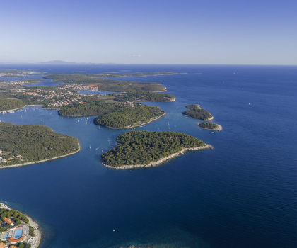 Aerial view of the coastline of Pjescana Uvala featuring lush green islands clear blue Adriatic Sea and scattered sailboats in Pula Istarska zupanija Croatia.