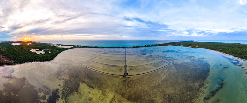 Aerial view of Salt Pond with geometric evaporation pans lush green vegetation and the turquoise ocean under a sunset sky Exuma Exuma The Bahamas.