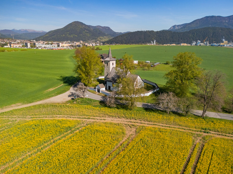 Aerial view of the historic All Saints Church surrounded by vibrant green and yellow fields with mountains in the distance Ludrova Zilina Region Slovakia. Aerial view of the historic All Saints Church surrounded by vibrant green and yellow fields with mountains in the distance Ludrova Zilina Region Slovakia.