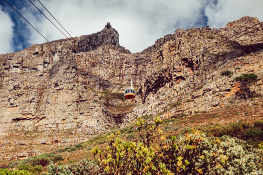 View of the Table Mountain Aerial Cableway car ascending the rugged rocky cliffs towards the summit under a cloudy sky in Cape Town Western Cape South Africa. View of the Table Mountain Aerial Cableway car ascending the rugged rocky cliffs towards the summit under a cloudy sky in Cape Town Western Cape South Africa.
