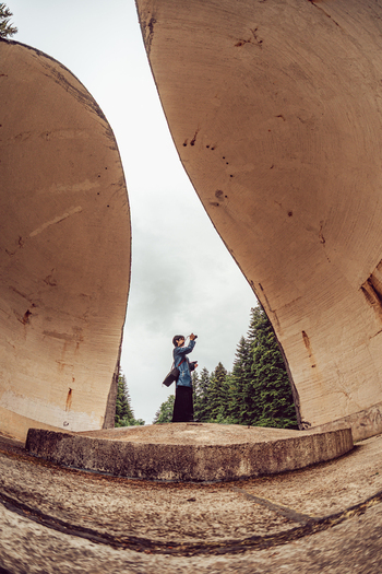 View of a person standing between the massive concrete wings of the Korcanica Memorial Zone surrounded by trees Sanski Most Federation of Bosnia Bosnia and Herzegovina. View of a person standing between the massive concrete wings of the Korcanica Memorial Zone surrounded by trees Sanski Most Federation of Bosnia Bosnia and Herzegovina.