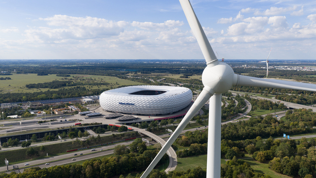 Munich Germany 11 September 2026 Aerial view of Allianz Arena surrounded by green fields highways and a wind turbine in the foreground under a blue sky. Munich Germany 11 September 2026 Aerial view of Allianz Arena surrounded by green fields highways and a wind turbine in the foreground under a blue sky.