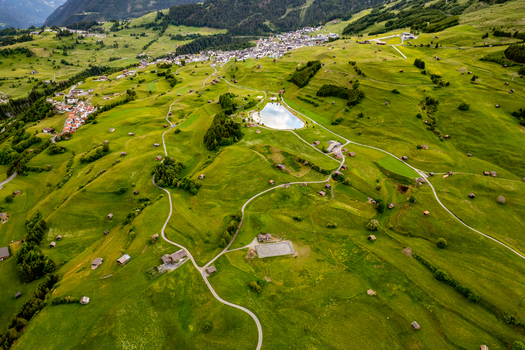 Aerial view of the village of Prutz in the Tyrol region of Austria featuring lush green alpine meadows small wooden huts winding roads and a small mountain lake. Prutz Tyrol Austria. Aerial view of the village of Prutz in the Tyrol region of Austria featuring lush green alpine meadows small wooden huts winding roads and a small mountain lake. Prutz Tyrol Austria.