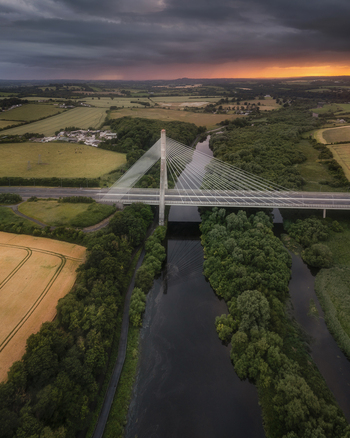 Aerial view of the Mary McAleese Boyne Valley Bridge spanning the river amidst lush green forests and fields under a dramatic sunset sky in Drogheda County Louth Ireland. Aerial view of the Mary McAleese Boyne Valley Bridge spanning the river amidst lush green forests and fields under a dramatic sunset sky in Drogheda County Louth Ireland.
