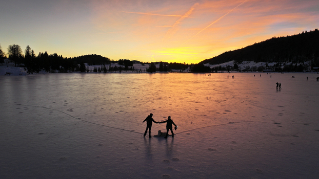 Aerial view of figures skating on the frozen lake with a backdrop of silhouettes of trees against the colorful sunset sky Les Rousses Bourgogne Franche Comté France. Aerial view of figures skating on the frozen lake with a backdrop of silhouettes of trees against the colorful sunset sky Les Rousses Bourgogne Franche Comté France.