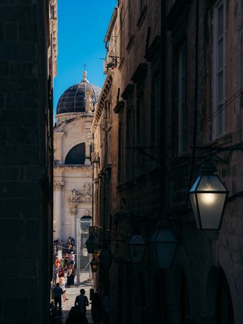 View of a narrow stone alleyway with traditional lanterns leading towards the Dubrovnik Cathedral dome under a clear blue sky in Dubrovnik Dubrovnik Neretva County Croatia. View of a narrow stone alleyway with traditional lanterns leading towards the Dubrovnik Cathedral dome under a clear blue sky in Dubrovnik Dubrovnik Neretva County Croatia.