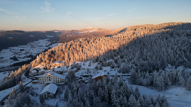 Aerial view of Col de la Faucille during winter featuring snow covered pine forests mountain slopes and alpine buildings under a clear sky in Gex Auvergne Rhone Alpes France. Aerial view of Col de la Faucille during winter featuring snow covered pine forests mountain slopes and alpine buildings under a clear sky in Gex Auvergne Rhone Alpes France.