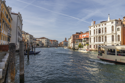 View of the Grand Canal in Venice with historic buildings a water bus and wooden mooring poles under a clear blue sky in Venice Veneto Italy. View of the Grand Canal in Venice with historic buildings a water bus and wooden mooring poles under a clear blue sky in Venice Veneto Italy.
