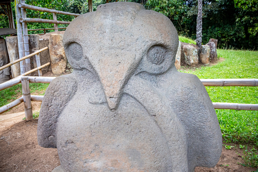 View of an ancient stone statue featuring intricate carvings and weathered texture in a lush green outdoor setting at the archaeological park San Agustin Huila Colombia.