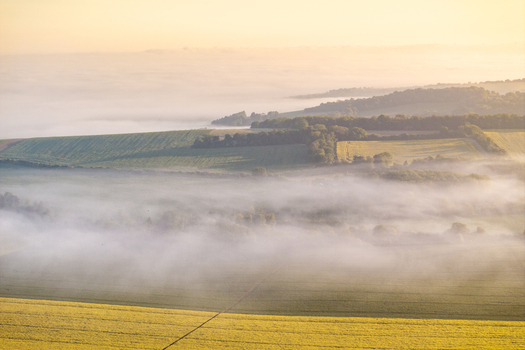 Aerial view of rolling green hills and agricultural fields covered in thick morning mist during a golden sunrise Nuffield Oxfordshire United Kingdom. Aerial view of rolling green hills and agricultural fields covered in thick morning mist during a golden sunrise Nuffield Oxfordshire United Kingdom.
