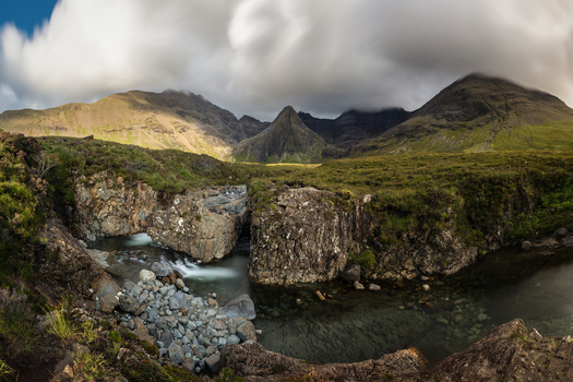 View of Fairy Pools with flowing water rocky cliffs and the Cuillin Mountains under dramatic clouds in Isle of Skye Scotland United Kingdom.