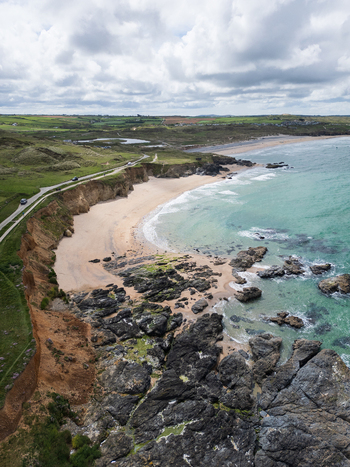 Aerial view of Godrevy Beach featuring turquoise waters rugged rocky outcrops and lush green cliffs under a cloudy sky in Gwithian England United Kingdom. Aerial view of Godrevy Beach featuring turquoise waters rugged rocky outcrops and lush green cliffs under a cloudy sky in Gwithian England United Kingdom.