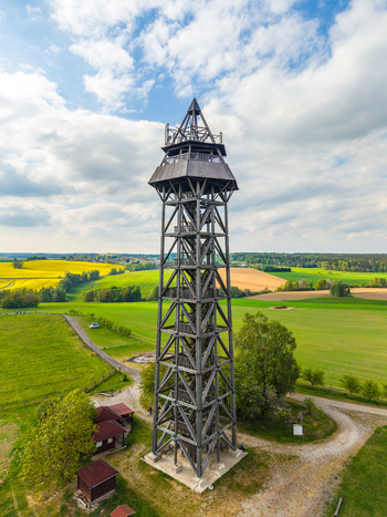 Aerial view of Bohdanka Lookout Tower surrounded by green fields and yellow rapeseed crops under a blue sky in Bohdanec Central Bohemian Region Czechia. Aerial view of Bohdanka Lookout Tower surrounded by green fields and yellow rapeseed crops under a blue sky in Bohdanec Central Bohemian Region Czechia.