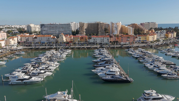 Aerial view of Vilamoura Marina with numerous luxury yachts docked in calm turquoise water surrounded by hotels and buildings in Quarteira Faro District Portugal.