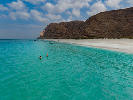 Aerial view of turquoise waters meet the pristine white sands near rugged cliffs as boats rest along the shore Shoab beach Socotra Yemen. Aerial view of turquoise waters meet the pristine white sands near rugged cliffs as boats rest along the shore Shoab beach Socotra Yemen.