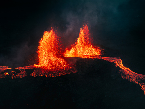 Aerial view of a volcanic eruption at night with glowing lava fountains and flowing molten rock streams against a dark landscape. Aerial view of a volcanic eruption at night with glowing lava fountains and flowing molten rock streams against a dark landscape.