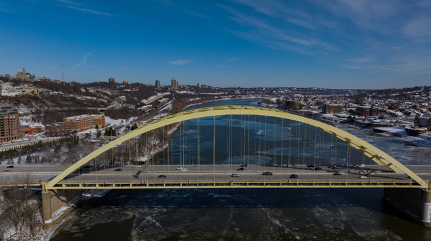 Aerial view of the yellow Daniel Carter Beard Bridge spanning the icy Ohio River with snow covered hills and urban buildings under a clear blue sky in Cincinnati Ohio United States. Aerial view of the yellow Daniel Carter Beard Bridge spanning the icy Ohio River with snow covered hills and urban buildings under a clear blue sky in Cincinnati Ohio United States.