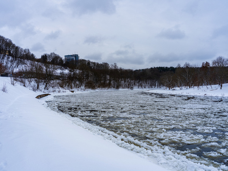 View of the frozen Neris River filled with ice floes surrounded by snow covered banks and bare trees under a cloudy winter sky in Vilnius Vilnius County Lithuania. View of the frozen Neris River filled with ice floes surrounded by snow covered banks and bare trees under a cloudy winter sky in Vilnius Vilnius County Lithuania.