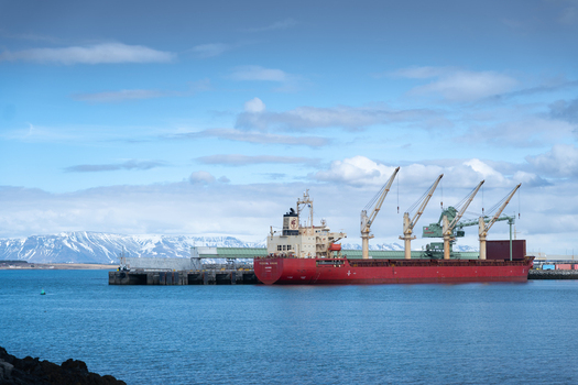 Hafnarfjordur Iceland 17 April 2026 View of a large red cargo ship docked at the port with industrial cranes and snow capped mountains under a blue sky.