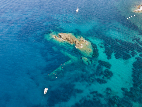 Aerial view of the Elviscot shipwreck submerged in clear turquoise waters near the rocky coast with swimmers and a small boat nearby in Pomonte Province of Livorno Italy.