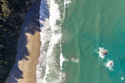 Aerial view of the southern Oregon coast featuring sandy beach crashing waves and offshore rocks in Gold Beach Oregon United States. Aerial view of the southern Oregon coast featuring sandy beach crashing waves and offshore rocks in Gold Beach Oregon United States.