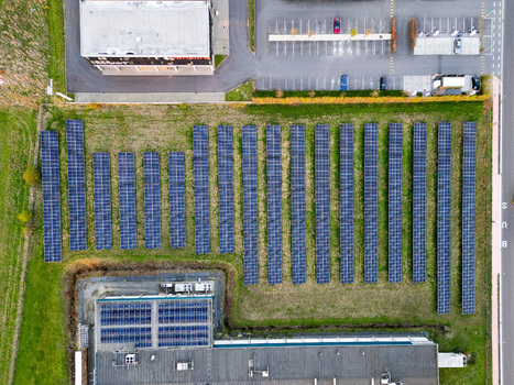 Aerial view of solar panels arrayed in neat rows casting deep blue shadows across the vibrant green field contrasting with the gray buildings Ath Wallonia Belgium. Aerial view of solar panels arrayed in neat rows casting deep blue shadows across the vibrant green field contrasting with the gray buildings Ath Wallonia Belgium.