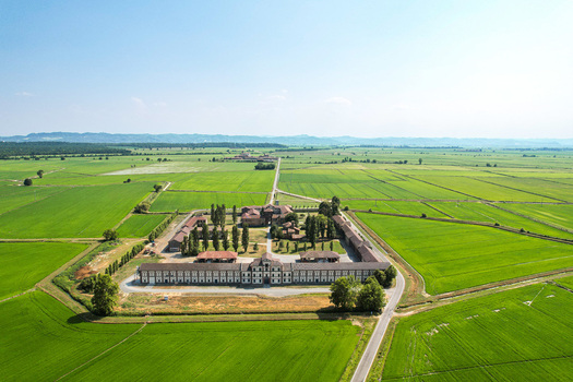 Aerial view of Tenuta Darola a historic estate surrounded by vast green rice fields under a clear blue sky in Trino Piemonte Italy. Aerial view of Tenuta Darola a historic estate surrounded by vast green rice fields under a clear blue sky in Trino Piemonte Italy.