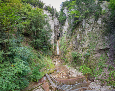 Aerial view of Grandvillard Waterfall cascading down a steep rocky cliff surrounded by dense green forest and a wooden walkway at the base Grandvillard Fribourg Switzerland.