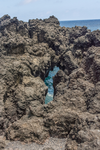 View of rugged volcanic rock formations along the coastline with the blue ocean visible through a gap in Maui County Hawaii United States.