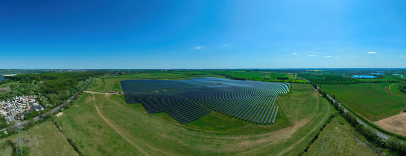 Aerial view of a large solar farm with rows of photovoltaic panels surrounded by green fields and trees under a clear blue sky in Little Irchester England United Kingdom. Aerial view of a large solar farm with rows of photovoltaic panels surrounded by green fields and trees under a clear blue sky in Little Irchester England United Kingdom.