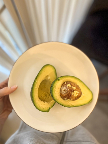 View of a fresh halved avocado with a brown pit served on a white ceramic plate held by a person in Beylikduzu Istanbul Turkiye. View of a fresh halved avocado with a brown pit served on a white ceramic plate held by a person in Beylikduzu Istanbul Turkiye.