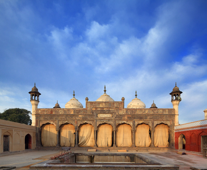 View of the historic Shahi Mosque with its ornate stone facade domes and minarets under a bright blue sky in Chiniot Punjab Pakistan.