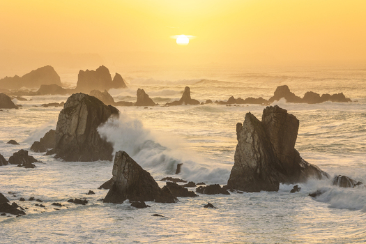 View of Silence Beach with jagged rock formations and crashing waves under a golden sunset in Asturias Asturias Spain.