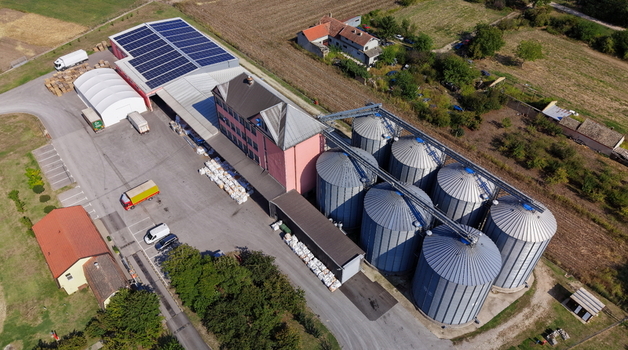 Aerial view of the silo Bavaniste grain storage facility featuring large metal silos a pink industrial building with solar panels and trucks in the yard in Bavaniste Vojvodina Serbia.