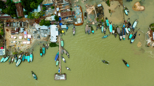 Aerial view of Baish Mowza Sarak Bazar with numerous wooden boats docked along the riverbank market stalls and rooftops in Nabinagar Chittagong Division Bangladesh. Aerial view of Baish Mowza Sarak Bazar with numerous wooden boats docked along the riverbank market stalls and rooftops in Nabinagar Chittagong Division Bangladesh.