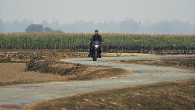 View of a man riding a motorcycle on a winding rural road Bangladesh.