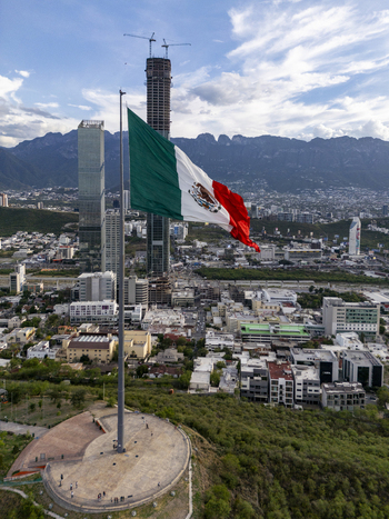 Aerial view of the Mexican flag flying on a tall flagpole with the Rise Tower under construction and the city skyline in the background Monterrey Nuevo Leon Mexico. Aerial view of the Mexican flag flying on a tall flagpole with the Rise Tower under construction and the city skyline in the background Monterrey Nuevo Leon Mexico.